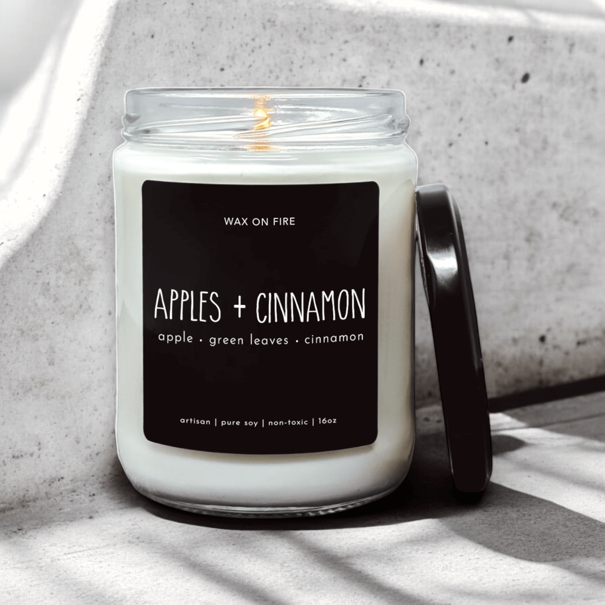 Apples + Cinnamon candle in a clear jar with a black lid, showcasing warm scent notes of apple and cinnamon.