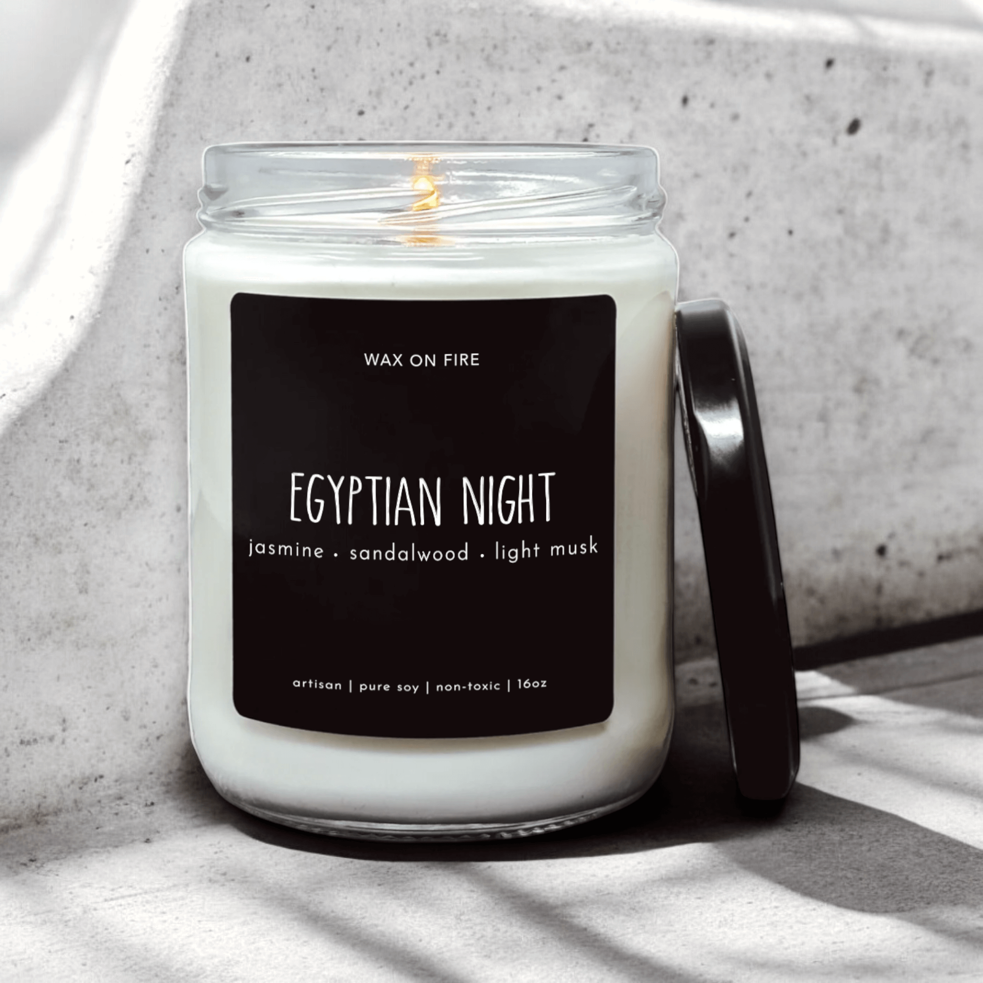 White artisan candle labeled 'Egyptian Night' with jasmine, sandalwood, and light musk scents on a concrete surface.