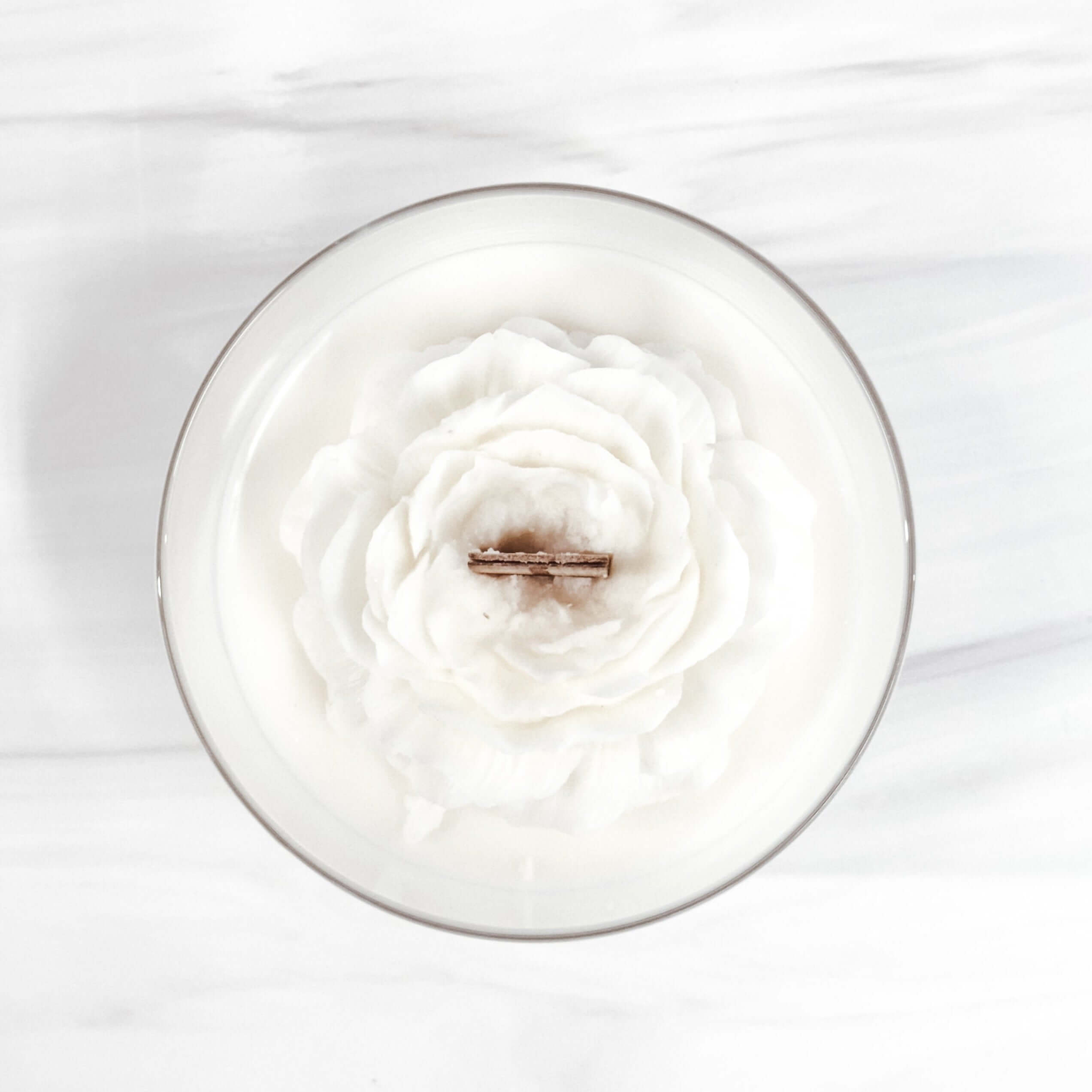 Peony flower candle in glass vessel with wood wick, showcasing a delicate floral design on a white wax surface.
