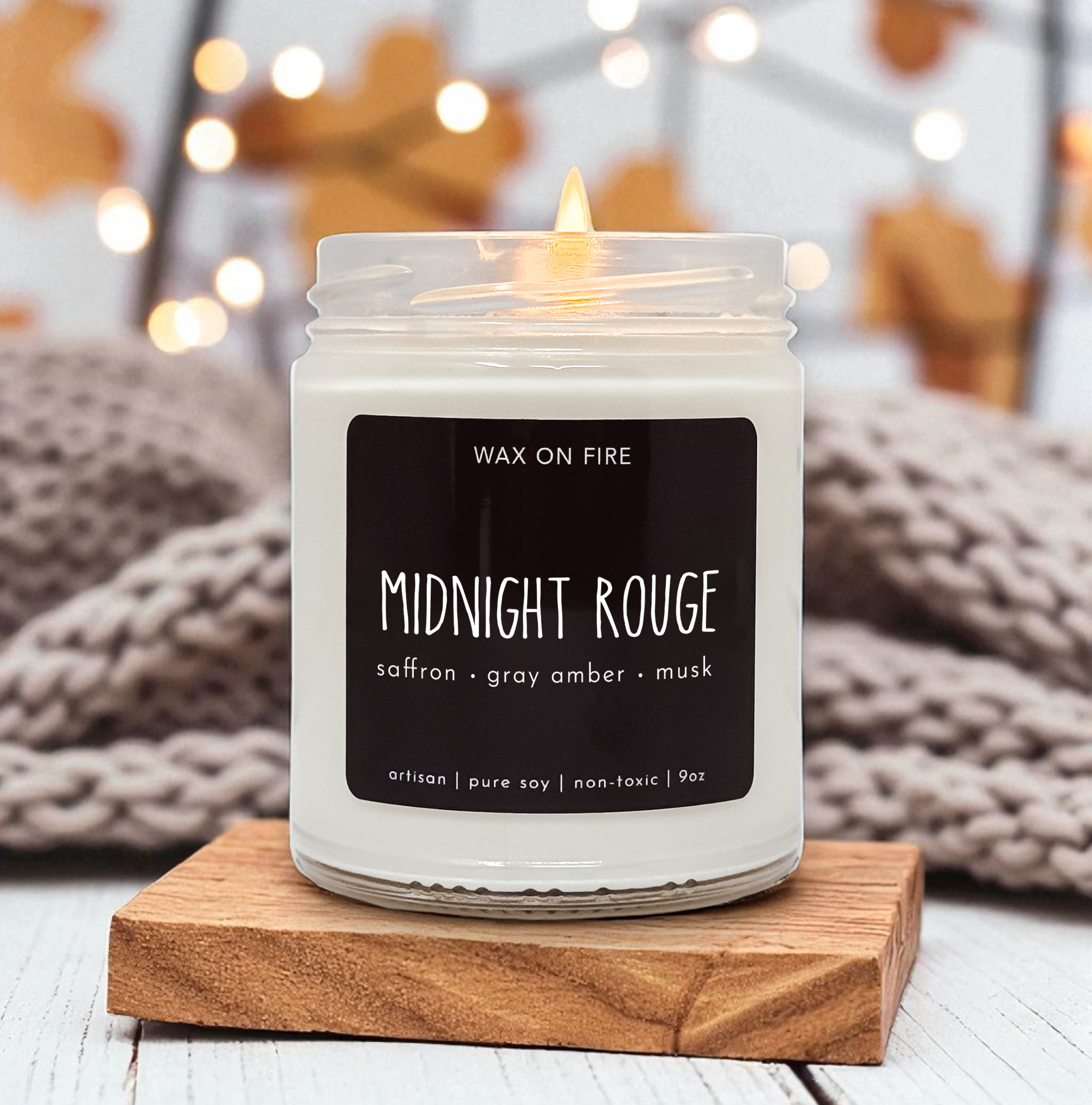 A white candle labeled "Midnight Romance" sits on a wooden coaster, with a blurred background featuring a cozy, warm atmosphere.