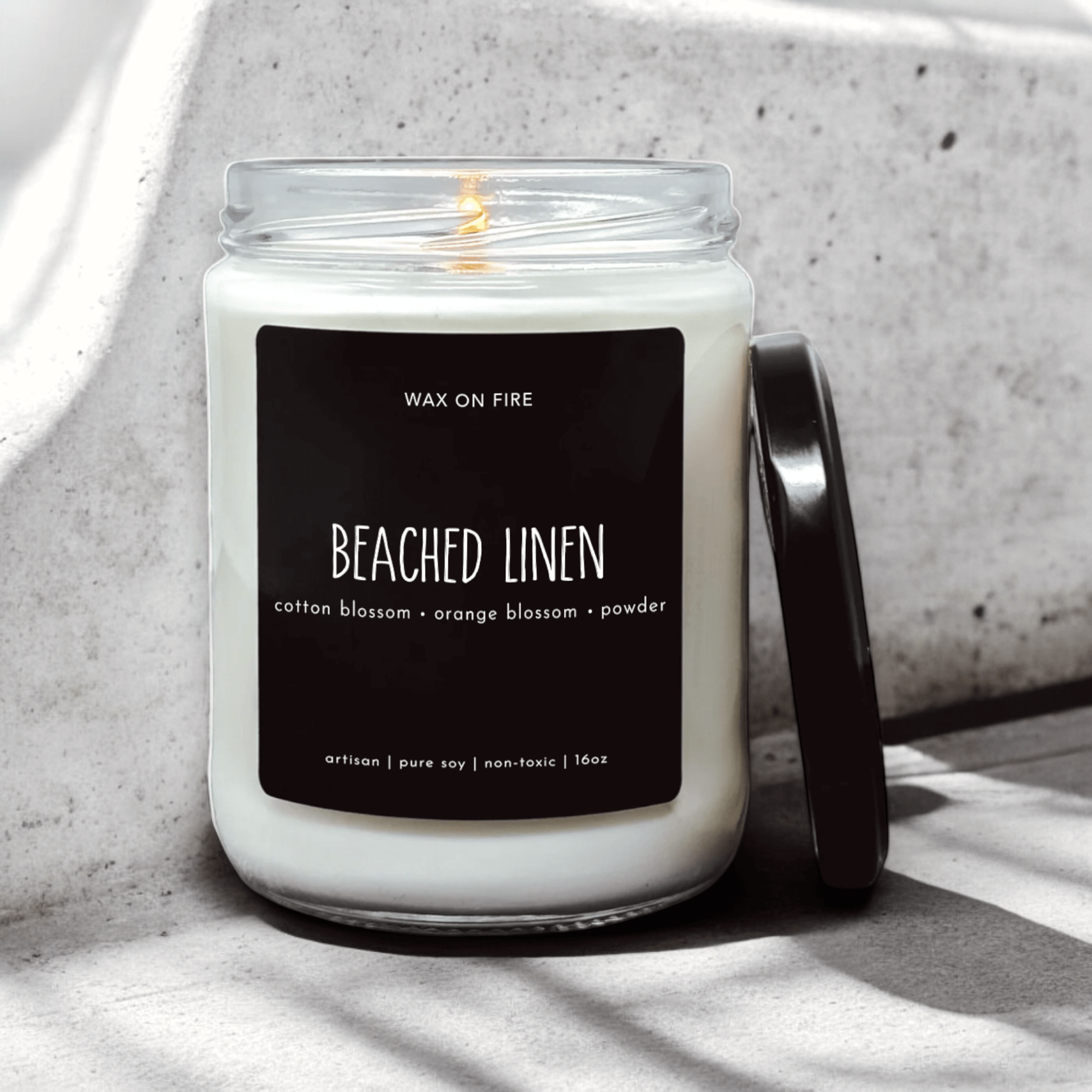 Beached Linen candle in a glass jar with black label featuring cotton and orange blossom scents.