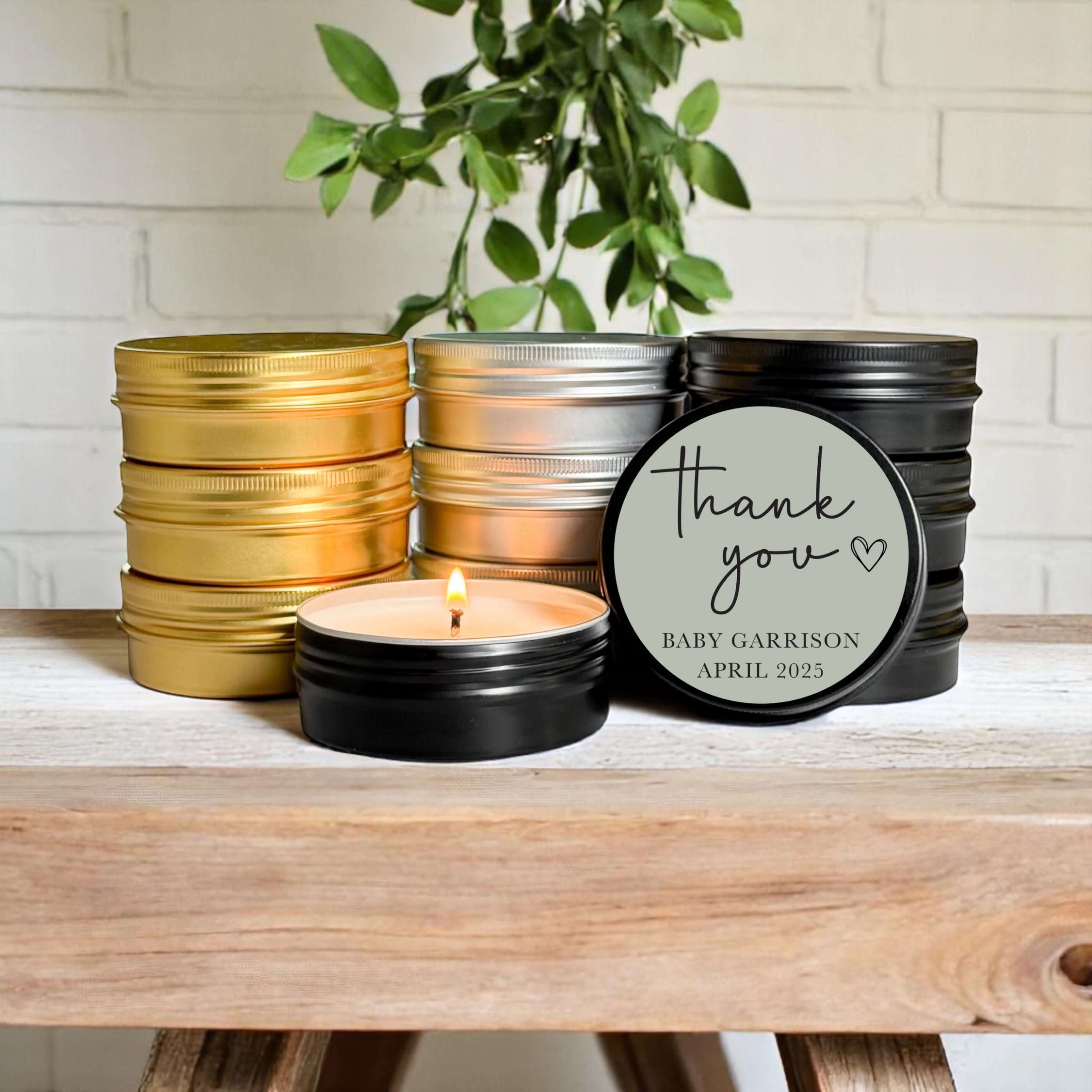 Bulk baby shower favors in stylish tins with candle, personalized label, and greenery background.