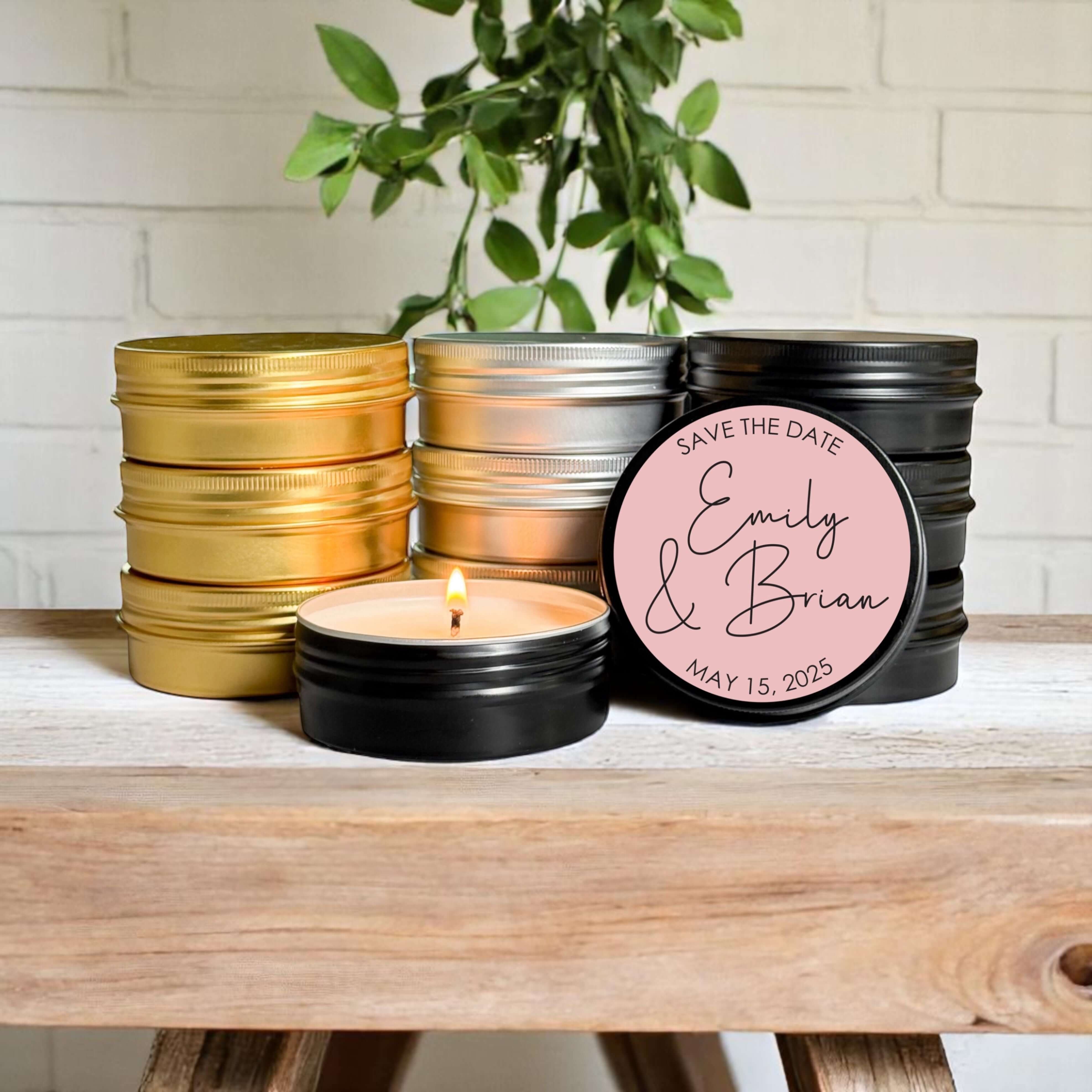 Bulk wedding favors with custom labels, featuring gold, silver, and black tins of hand-poured candles on a rustic table.