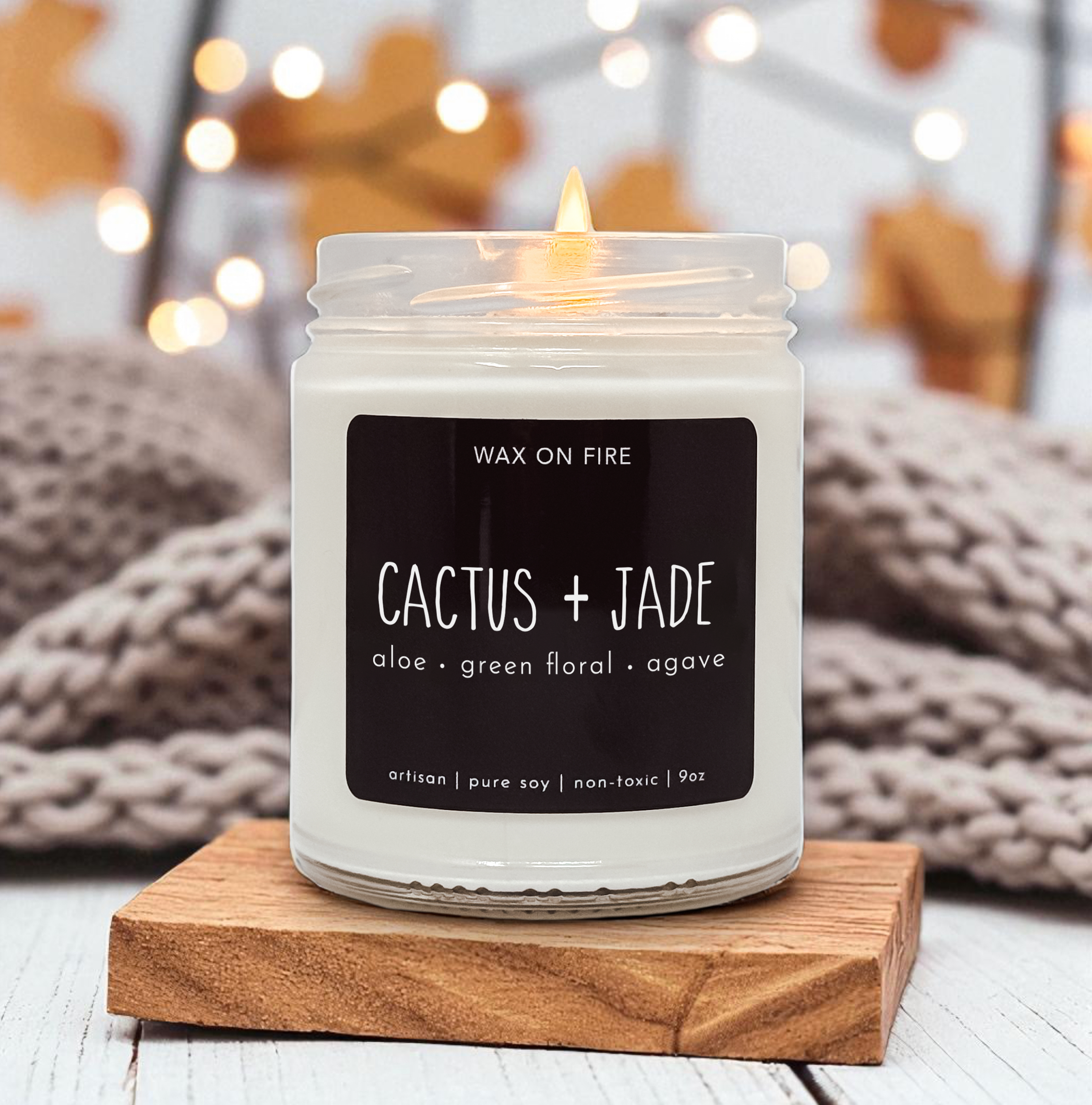 A white candle labeled "Wax on Fire" sits on a wooden coaster, with a blurred background featuring a cozy, warm atmosphere.