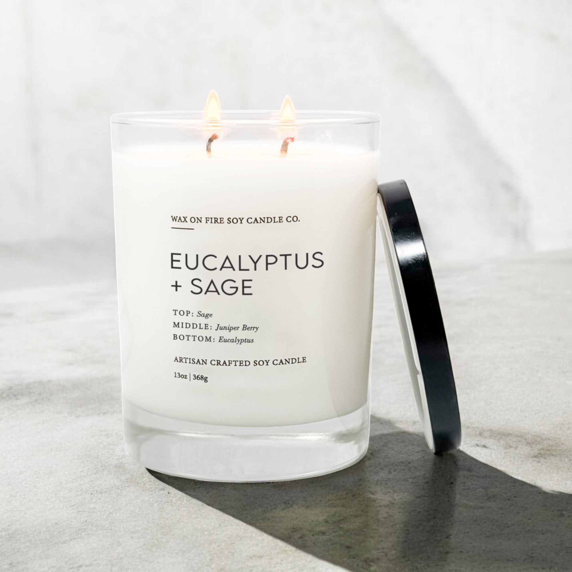 Eucalyptus + Sage 2-wick candle in a glass jar with two flames, featuring herbal and fresh scent notes.