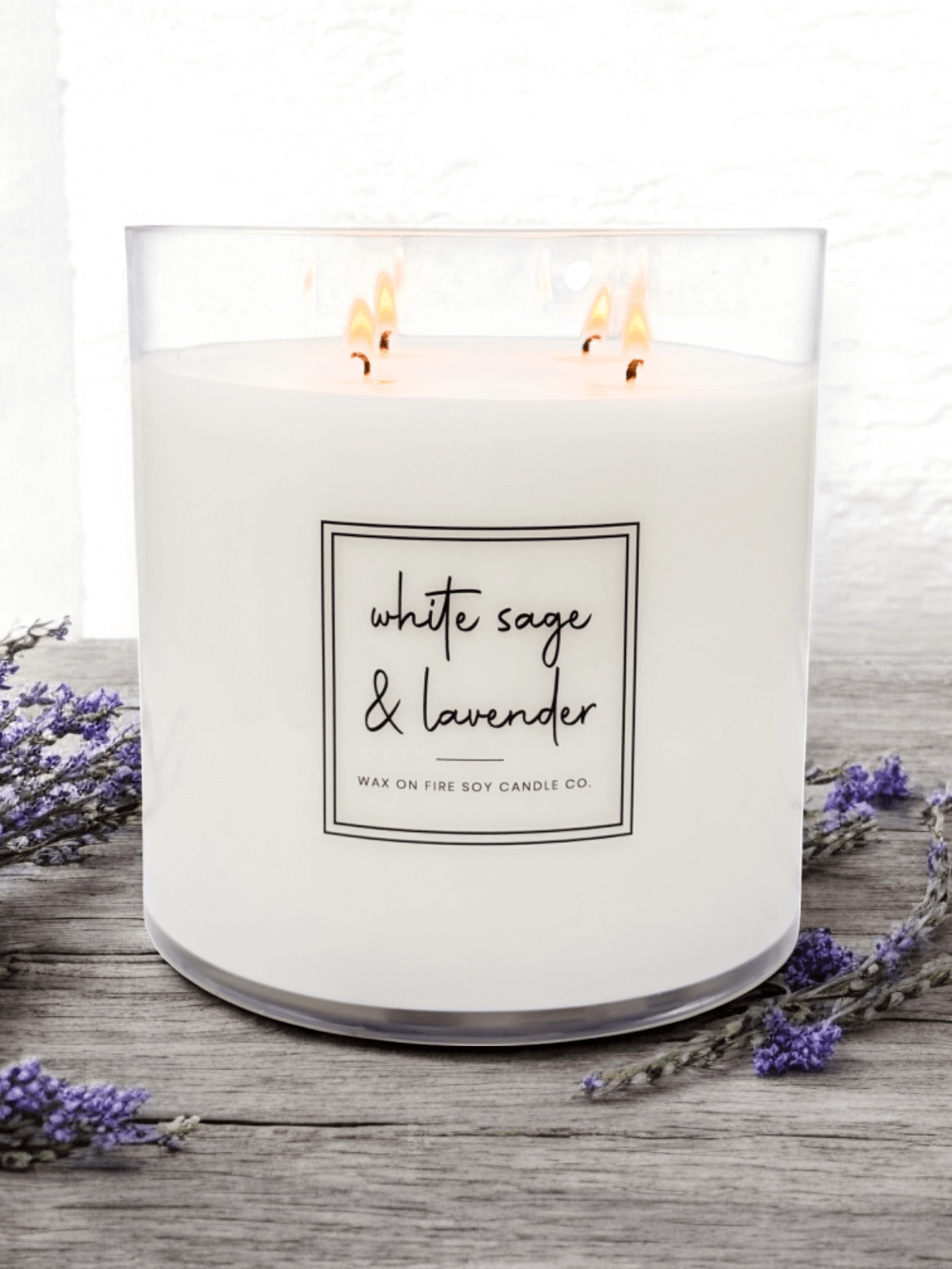 Signature 4-wick candle with white sage and lavender scent surrounded by lavender flowers.